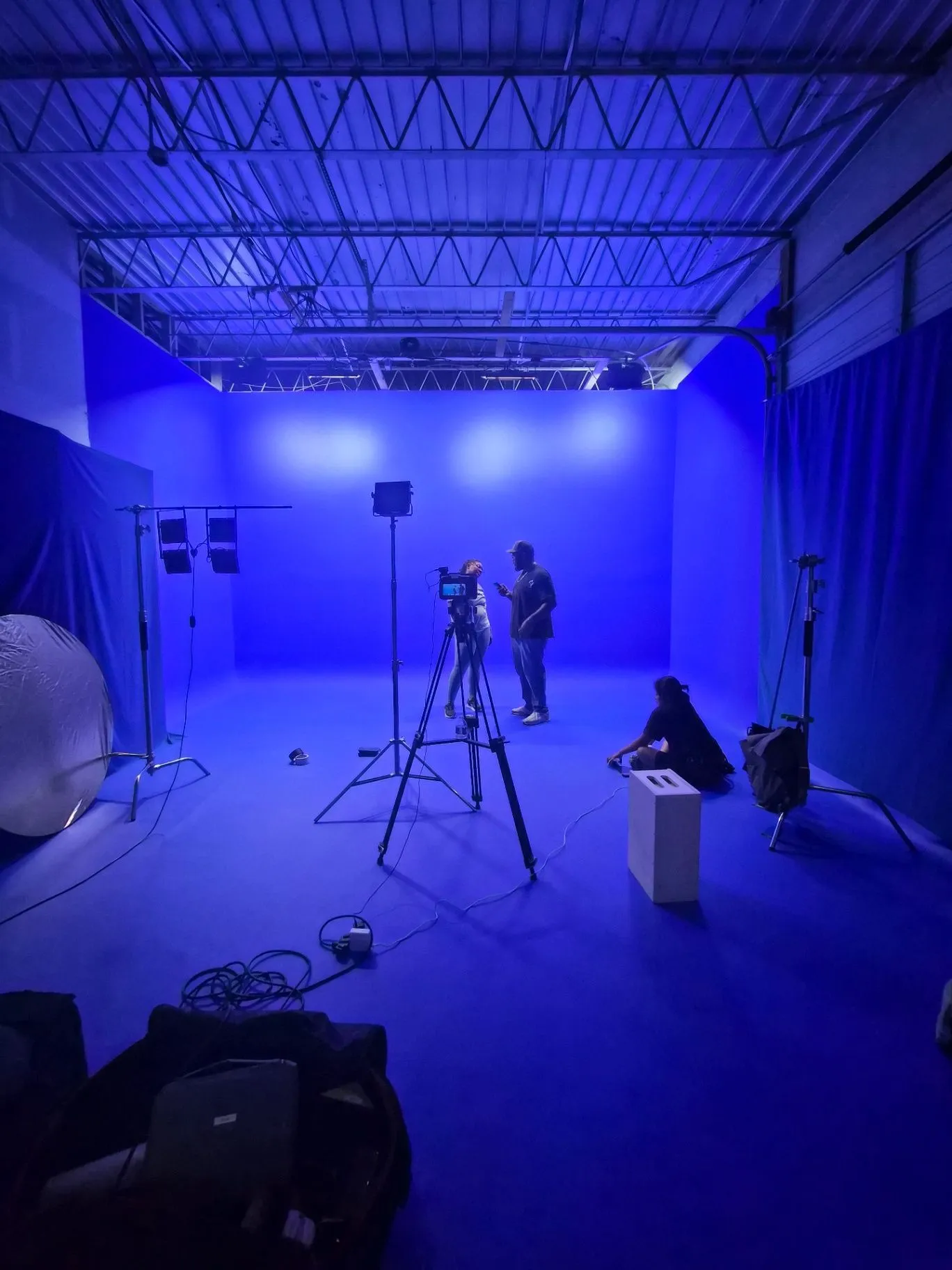 Crew, camera, lighting stands, and cables arranged on the blue cyclorama during production