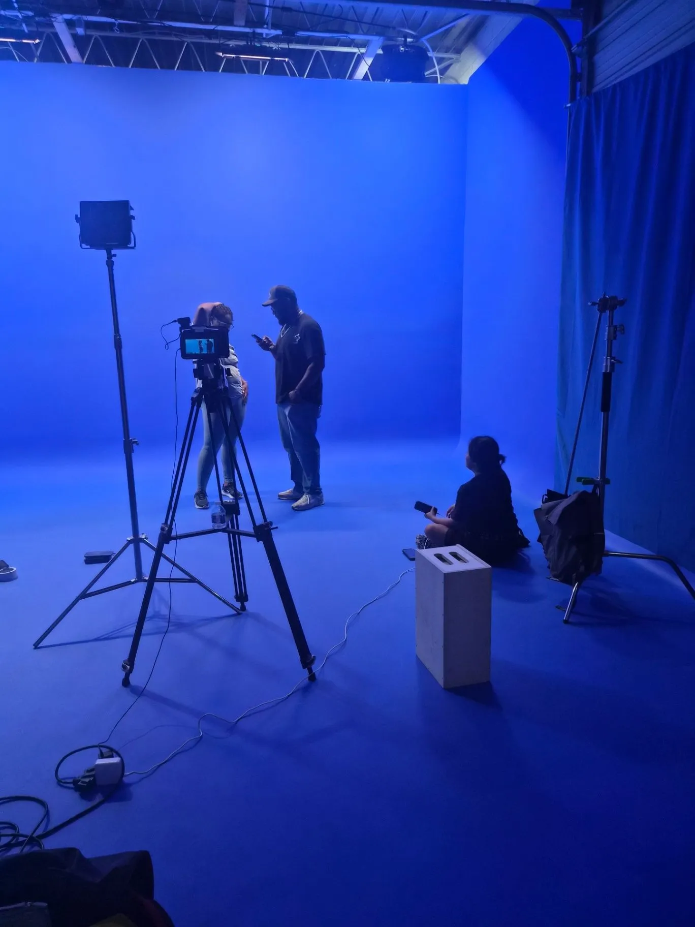 Crew gathered around a camera on the blue cyclorama with a light and production gear in view